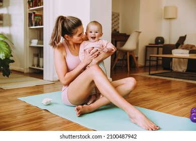 Adorable Baby Smiling Excitedly In Her Mother's Arms. Happy Mother Working Out With Her Baby On An Exercise Mat. Loving New Mom Bonding With Her Baby During Her Post-natal Fitness Routine.