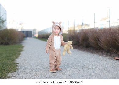 Adorable baby wearing teddy bear costume holding his animal doll standing outdoor background. Mixed race Asian-German infant boy with warm clothes playing outside. Fashion kid clothes. - Powered by Shutterstock