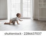 Adorable baby wearing white bodysuit, crawling on knees on floor at home. Curious active little infant child learning to move on warm heating safe floor, passing by window in background