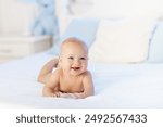 Adorable baby in white sunny bedroom. Newborn child relaxing in bed. Nursery for young children. Textile and bedding for kids. Family morning at home. New born kid during tummy time with toy bear.