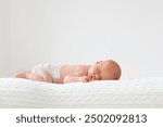 Adorable baby in white sunny bedroom. Newborn child relaxing in bed. Nursery for young children. Textile and bedding for kids. Family morning at home. New born kid during tummy time with toy bear.