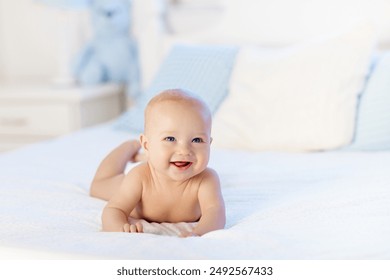 Adorable baby in white sunny bedroom. Newborn child relaxing in bed. Nursery for young children. Textile and bedding for kids. Family morning at home. New born kid during tummy time with toy bear.