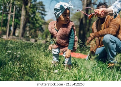 Adorable Black Girl Enjoys Playing In A Park Or Garden During A Walk Outside With Her Family. Funny African American Toddler Playing Outdoor. Spending Day In The Park With A Family.