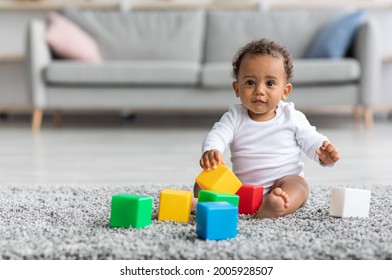 Adorable Black Infant Baby Playing With Stacking Building Blocks At Home While Sitting On Carpet In Living Room, Portrait Of Cute African American Child Using Colorful Constructor Toys, Copy Space