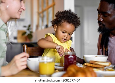 Adorable Black Toddler Girl Enjoying Breakfast With Parents At Home, Pretty Child Eating Porridge. Healthy Food For Young Children. Interracial Family At Home At Weekends, Holidays, In The Morning