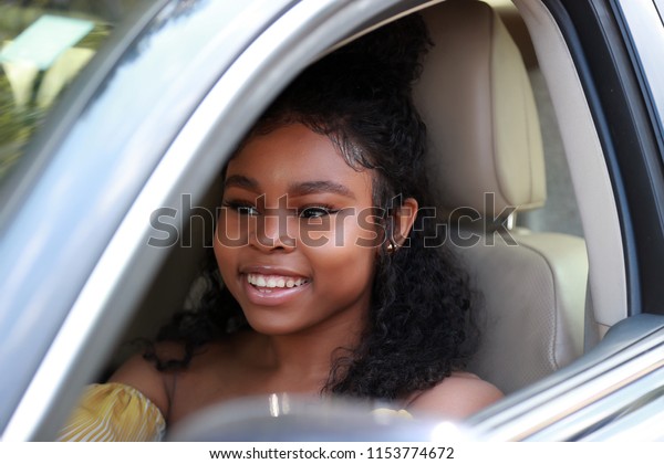 Adorable black woman with curls driving car\
with smile looking away with window\
opened