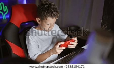 Adorable blond boy streamer, engrossed in serious game playing, live streaming his smartphone game from a cozy gaming room