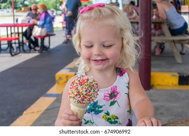 Adorable Blonde Girl Eating Ice Cream Cone Covered With Sprinkles