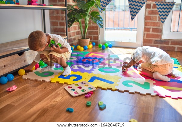Adorable blonde twins playing with cars\
around lots of toys at\
kindergarte