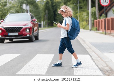 Adorable boy with a backpack, headphones and cellphone goes through the pedestrian crossing, not looking at red cars let him through - Powered by Shutterstock