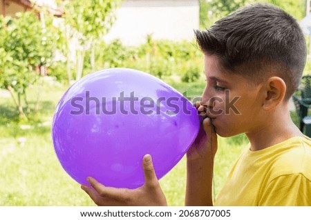 Adorable boy blowing up balloon for a birthday. Portrait of a boy inflating a purple balloon in the garden of the house Foto stock © 