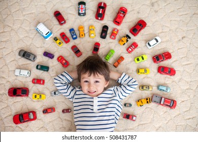 Adorable boy, lying on the ground, toy cars around him , looking at the camera, shot from above