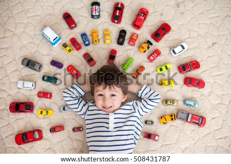 Adorable boy, lying on the ground, toy cars around him , looking at the camera, shot from above