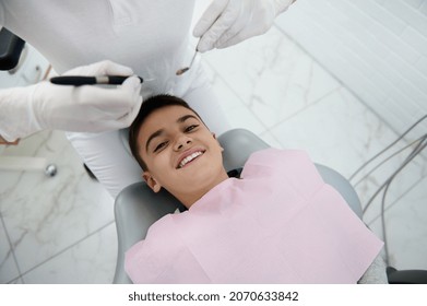 Adorable brave handsome preadolescent boy in dentist's chair smiles toothy smile looking at camera and waiting for dental examination and treatment in modern dental office. Close-up. Top view - Shutterstock ID 2070633842
