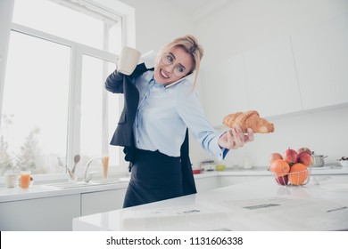 Adorable busy attractive charming beautiful smiling lady office executive worker wearing spectacles in hurry early in the morning talking on the phone having a drink and croissant in kitchen