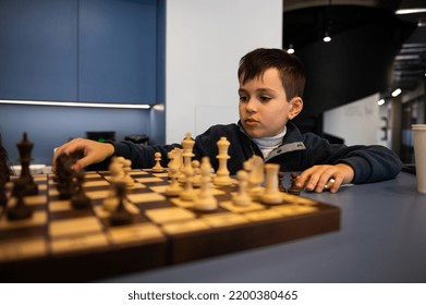 Adorable Caucasian 10 Years Old Child, Smart School Boy Sitting At A Table And Playing Chess, Thoughtfully Moving A Chess Piece On A Chessboard. Board Games For Kids Entertainment And Development