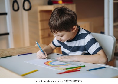 adorable caucasian boy of elementary age drawing a rainbow with pencils sitting at the desk in his room at home. Image with selective focus - Shutterstock ID 1926880022