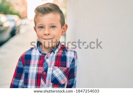 Adorable caucasian boy smiling happy leaning on the wall at the city.