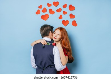 adorable caucasian couple stand hugging, wearing tuxedo and dress. nice man and woman after a date. redhaired lady hold one red rose in hand stand with closed eyes, isolated over blue background - Shutterstock ID 1637415736