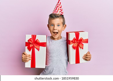 Adorable Caucasian Kid Wearing Birthday Hat Holding Presents Celebrating Crazy And Amazed For Success With Open Eyes Screaming Excited. 