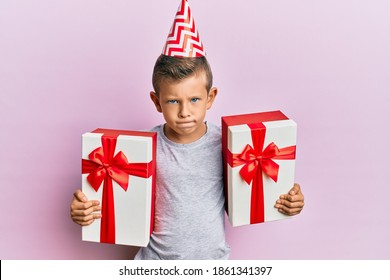 Adorable Caucasian Kid Wearing Birthday Hat Holding Presents Skeptic And Nervous, Frowning Upset Because Of Problem. Negative Person. 