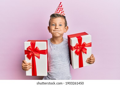 Adorable Caucasian Kid Wearing Birthday Hat Holding Presents Puffing Cheeks With Funny Face. Mouth Inflated With Air, Catching Air. 