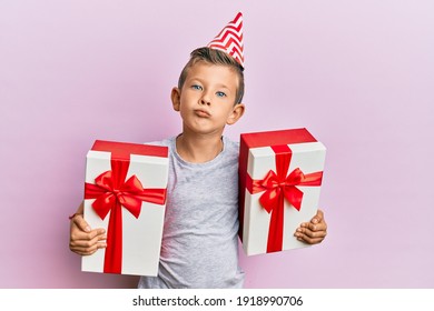 Adorable Caucasian Kid Wearing Birthday Hat Holding Presents Looking At The Camera Blowing A Kiss Being Lovely And Sexy. Love Expression. 