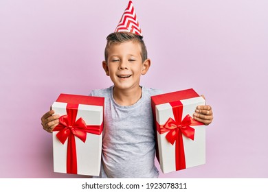 Adorable Caucasian Kid Wearing Birthday Hat Holding Presents Smiling And Laughing Hard Out Loud Because Funny Crazy Joke. 