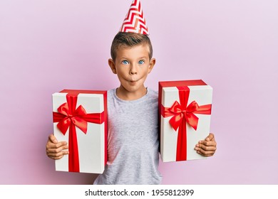 Adorable Caucasian Kid Wearing Birthday Hat Holding Presents Making Fish Face With Mouth And Squinting Eyes, Crazy And Comical. 