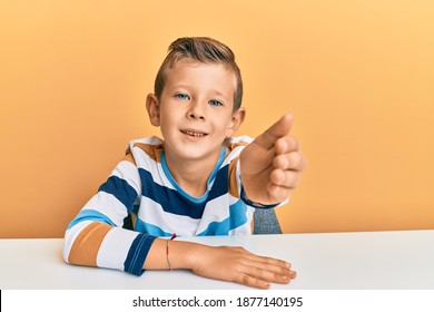 Adorable caucasian kid wearing casual clothes sitting on the table smiling friendly offering handshake as greeting and welcoming. successful business.  - Powered by Shutterstock