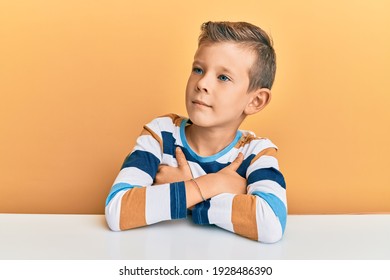 Adorable Caucasian Kid Wearing Casual Clothes Sitting On The Table Looking To The Side With Arms Crossed Convinced And Confident 