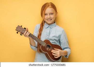 Adorable Caucasian Teen Girl With Natural Red Hair Holding Ukulele In Hands, She Enjoy Playing In Such Unusual Type Of Instruments Ukulele, Small Guitar. Music, People, Children Concept