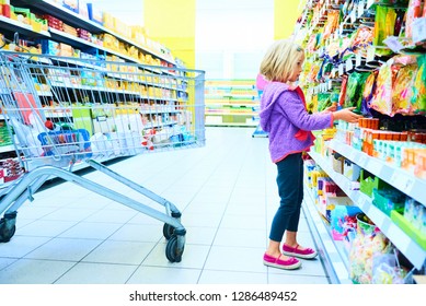 Adorable child blond girl select sweets on shelves in supermarket 