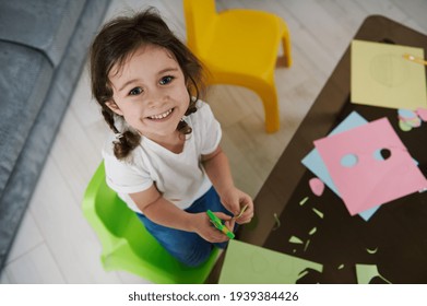 Adorable Child Holding Scissors, Cutting Color Paper And Cute Smiles To The Camera. Creative Hobby. Cute Little Girl With Color Paper