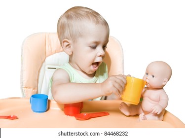 Adorable child independently feeding doll sitting in front of the table. Kid's role playing in two years. Over white