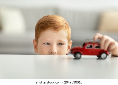 Adorable Child Playing With Red Car Toy On White Table, Cute Redhead Kid Schooler Boy Playing With Vehicles At Home, Riding Small Vintage Automobile By Surface. Kids Toys And Entertainment Concept