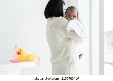 Adorable Cold African Newborn Baby Was In Mother's Embrace After Bathing In Bathtub. Asian Young Mother Wrap Up Her Little Daughter Warm In Towel At Bathroom. Newborn Baby Cleanliness Care Concept