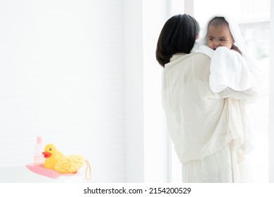 Adorable Cold African Newborn Baby Was In Mother's Embrace After Bathing In Bathtub. Asian Young Mother Wrap Up Her Little Daughter Warm In Towel At Bathroom. Newborn Baby Cleanliness Care Concept