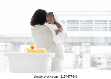 Adorable Cold African Newborn Baby Was In Mother's Embrace After Bathing In Bathtub. Asian Young Mother Wrap Up Her Little Daughter Warm In Towel At Bathroom. Newborn Baby Cleanliness Care Concept