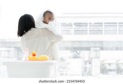 Adorable Cold African Newborn Baby Was In Mother's Embrace After Bathing In Bathtub. Asian Young Mother Wrap Up Her Little Daughter Warm In Towel At Bathroom. Newborn Baby Cleanliness Care Concept