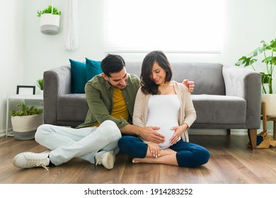 Adorable couple sitting on their living room floor and caressing the belly of the pregnant woman. Caring husband talking to her pregnant wife's belly