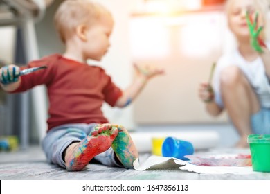 Adorable Cute Caucasian Little Blond Siblings Children Enjoy Having Fun Painting With Brush And Palm At Home Indoors . Cheerful Happy Kids Smiling Drawing Masterpiece Art Picture. Messy Dirty Room