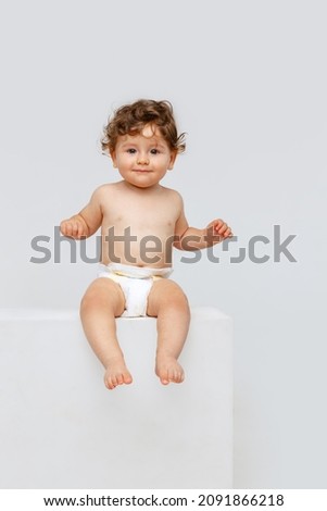 Adorable, cute child. Portrait of little sweet toddler boy, baby in diaper calmly sitting isolated over white studio background. Concept of childhood, motherhood, life, birth. Copy space for ad