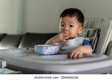adorable and cute happy Asian Chinese baby boy siting on baby chair enjoying meal with dirty face