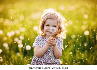 Adorable cute little baby girl blowing on a dandelion flower on the nature in the summer. Happy healthy beautiful toddler child with blowball, having fun. Bright sunset light, active kid. - Powered by Shutterstock