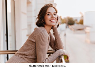 Adorable dark-eyed girl laughing at balcony. Photo of cheerful caucasian woman with beautiful smile.