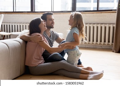 Adorable Daughter Spend Time With Loving Mom And Dad Family In Home Clothes Lean On Couch Sit On Warm Wooden Floor With Underfloor Heating Feel Comfort Having Fun Talking Enjoy Communication Together