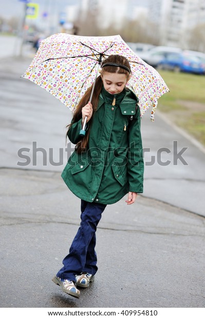 Adorable, elegant school\
aged kid  girl ,holding colorful umbrella walking in the city\
street in rainy day
