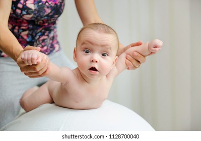 Adorable emotional baby boy  during massage by therapist. How massaging your baby helps development. Exercises on a ball to strengthen baby body