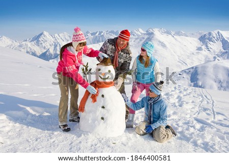 An adorable family having fun while building and decorating a snowman together in front of a magnificent range of snow mountains
